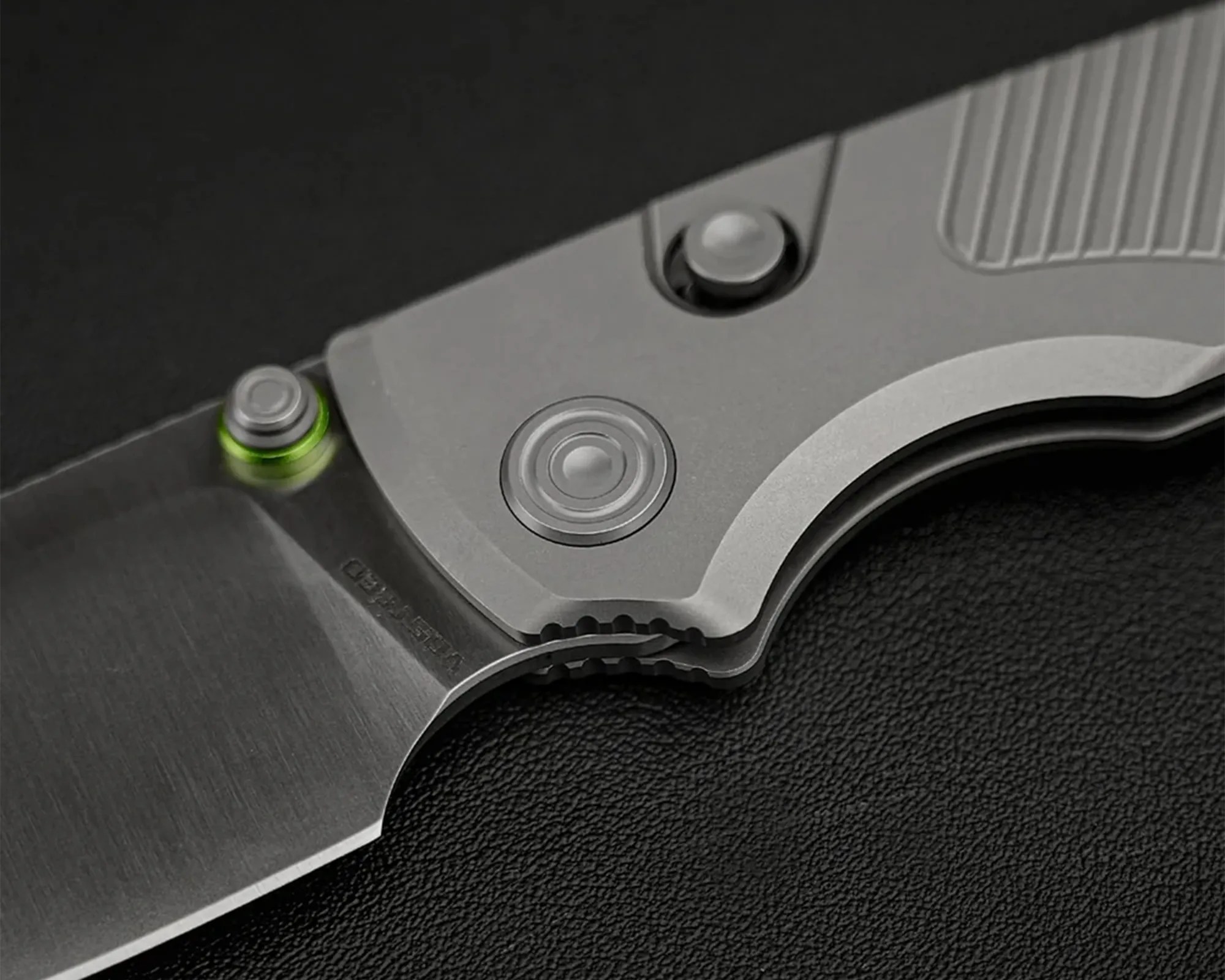 Close-up of a folding knife with a gray metal handle and a partially visible blade on a black textured surface.