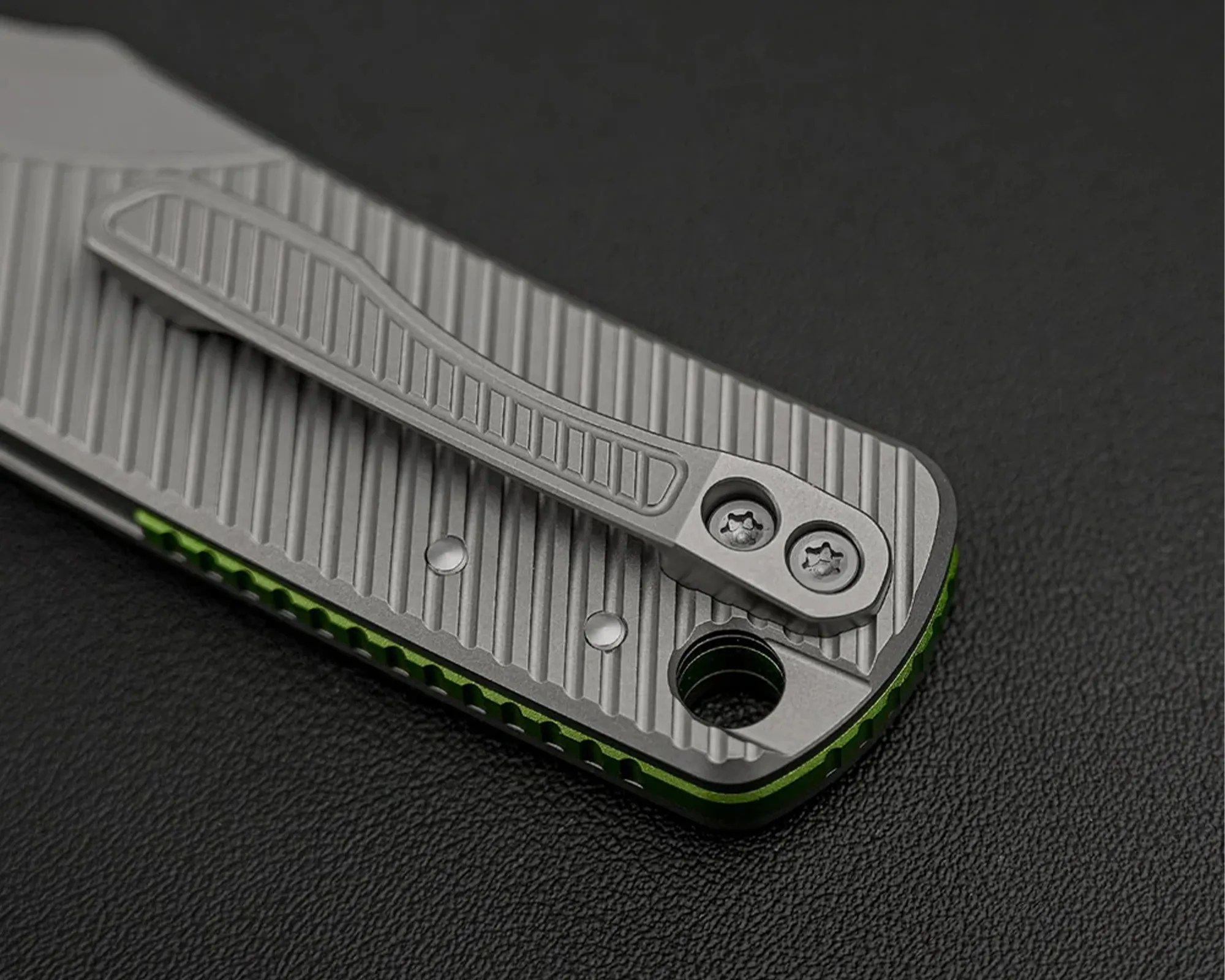 Close-up of a gray metal pocket clip with textured grooves attached to a green and gray folding knife handle.