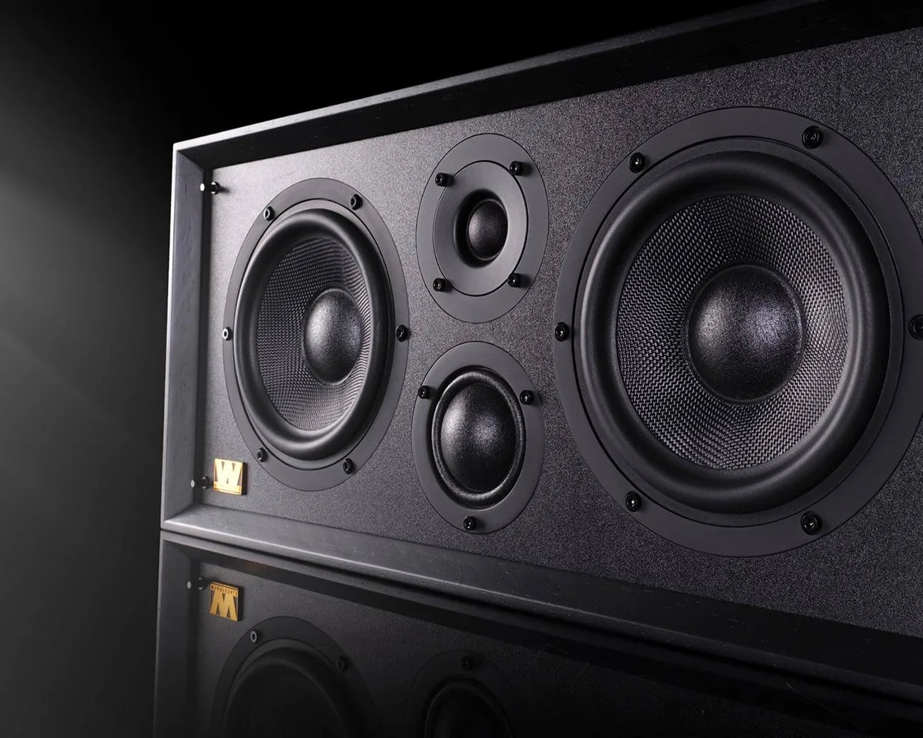Black rectangular speaker with four drivers and a small gold "W" logo on the bottom left corner.