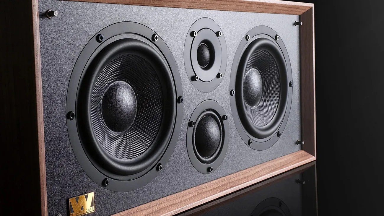 Rectangular speaker with two large black woofers, two smaller tweeters, and a wooden frame on a reflective black surface.