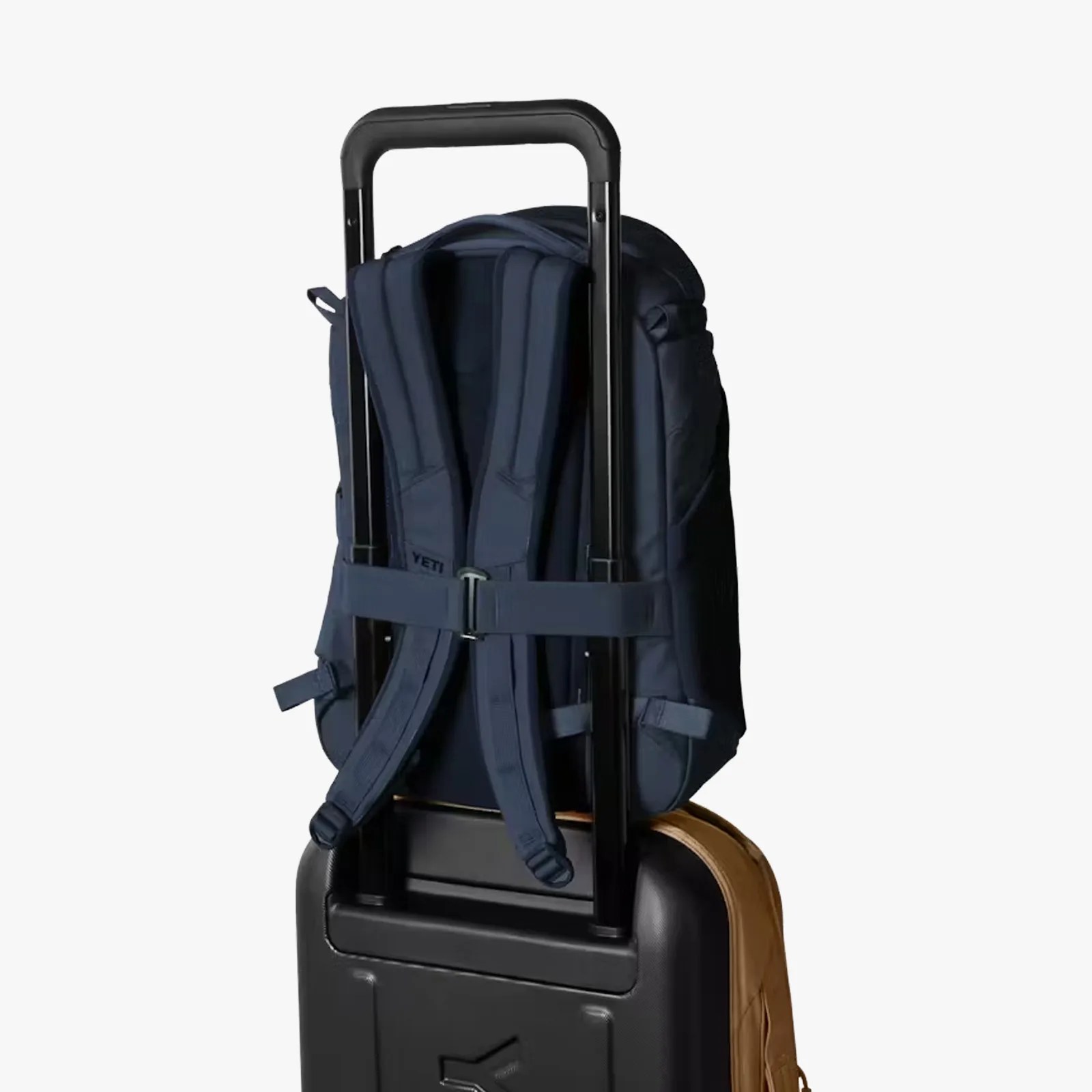 Navy blue backpack secured on the handle of a black rolling suitcase.