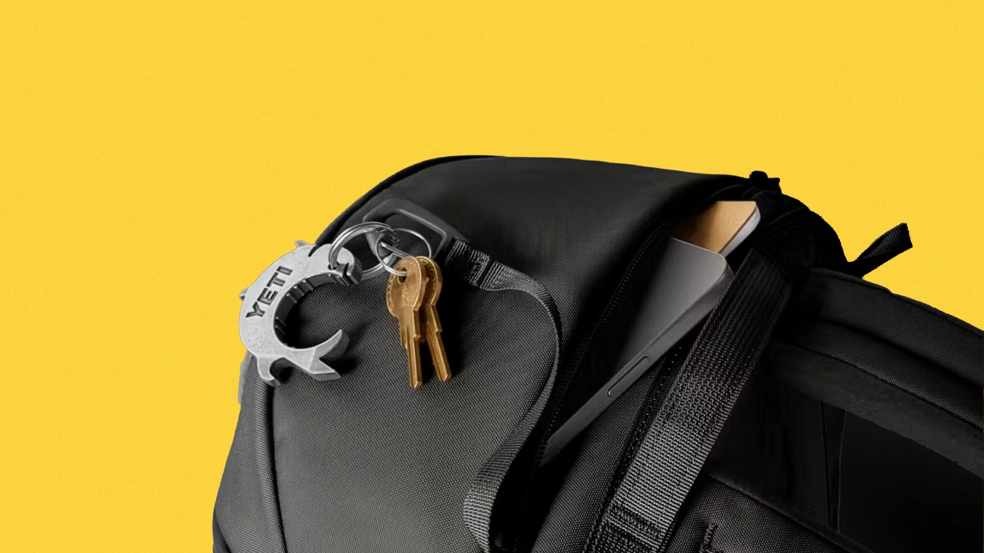 Black backpack with a partially open zipper revealing a laptop and notebook, with keys and a silver YETI keychain attached.