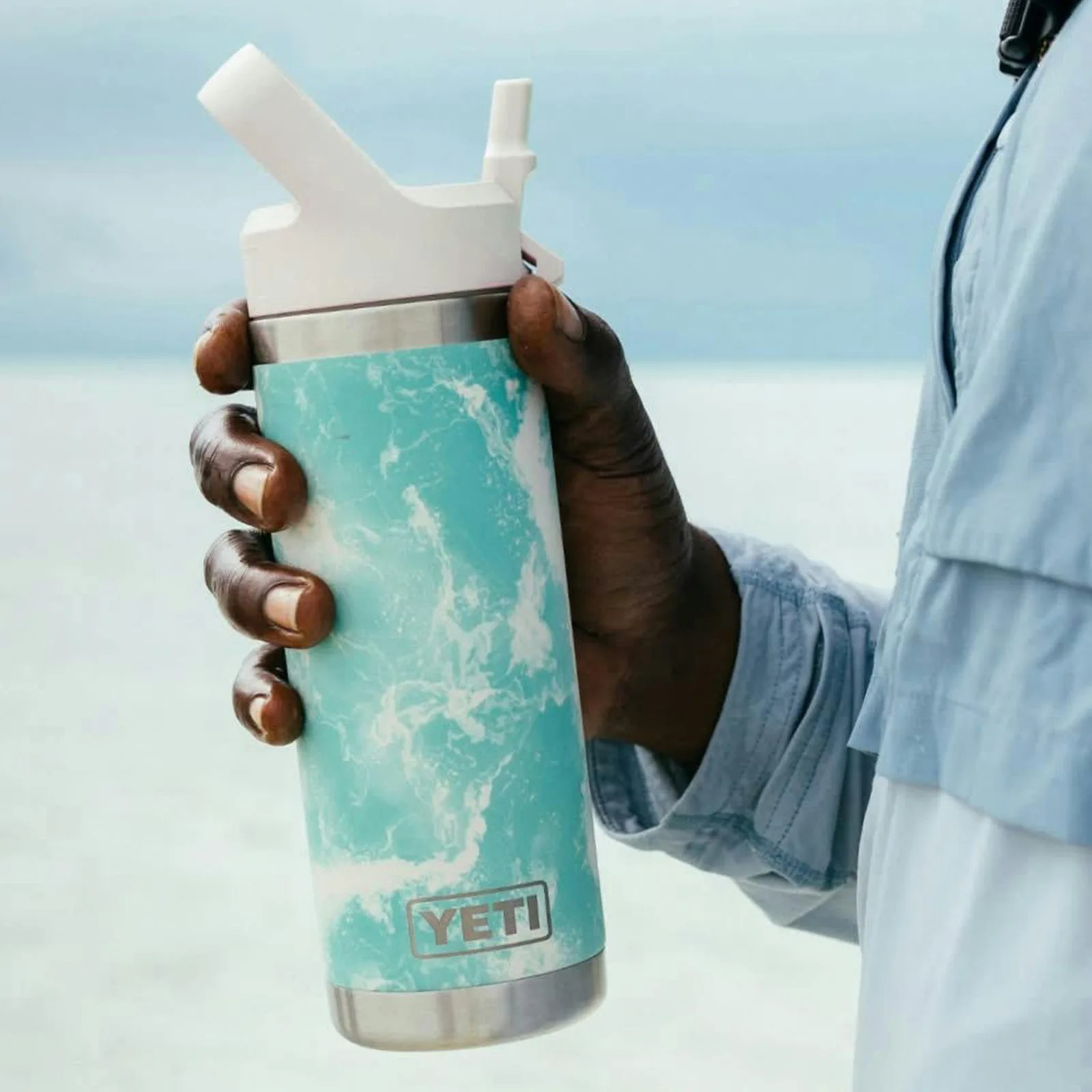 Hand holding a turquoise and white marbled YETI tumbler with a white lid.