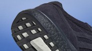 Close-up of the black sneaker sole with white cushioning and textured knit upper against a blue background.