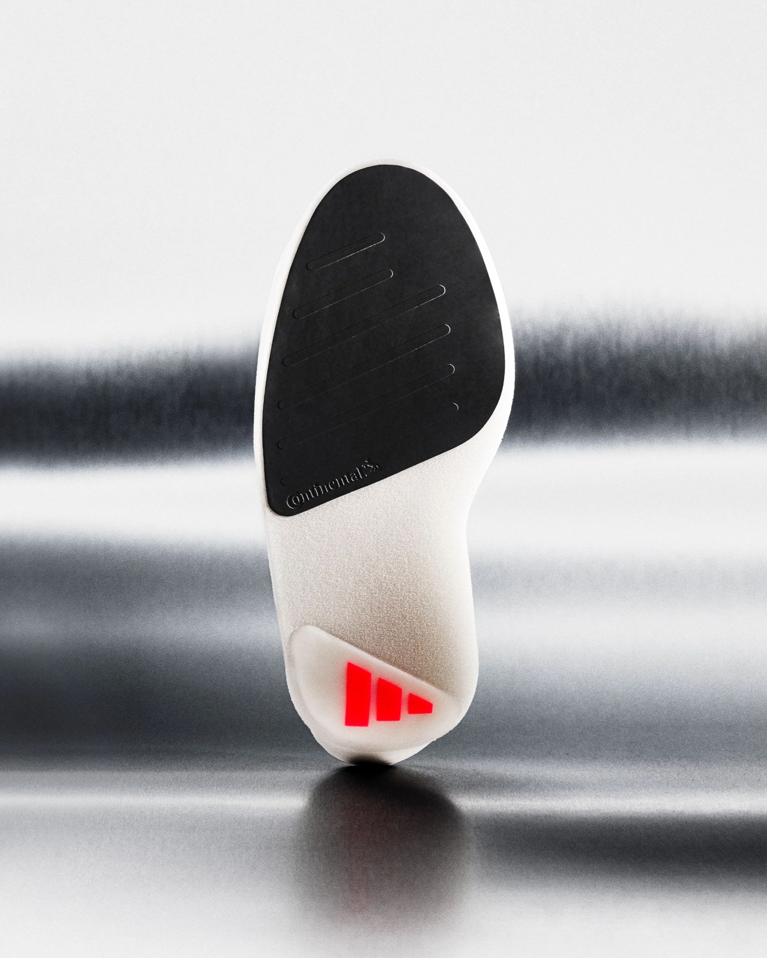 Close-up of a white shoe sole with a black Continental rubber grip and red logo on a reflective surface.