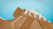 Close-up of a tan leather sneaker with white laces against a blue background.