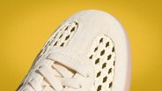Close-up of the toe area of a cream-colored sneaker with woven mesh panels and matching laces against a yellow background.