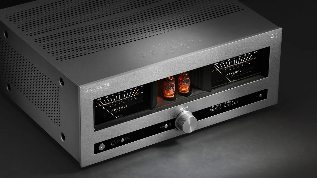 Silver Advance Paris AI 110 audio amplifier with volume knob, two glowing vacuum tubes, and analog meters on a dark surface.