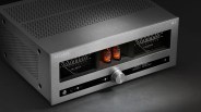 Silver Advance Paris AI 110 audio amplifier with volume knob, two glowing vacuum tubes, and analog meters on a dark surface.