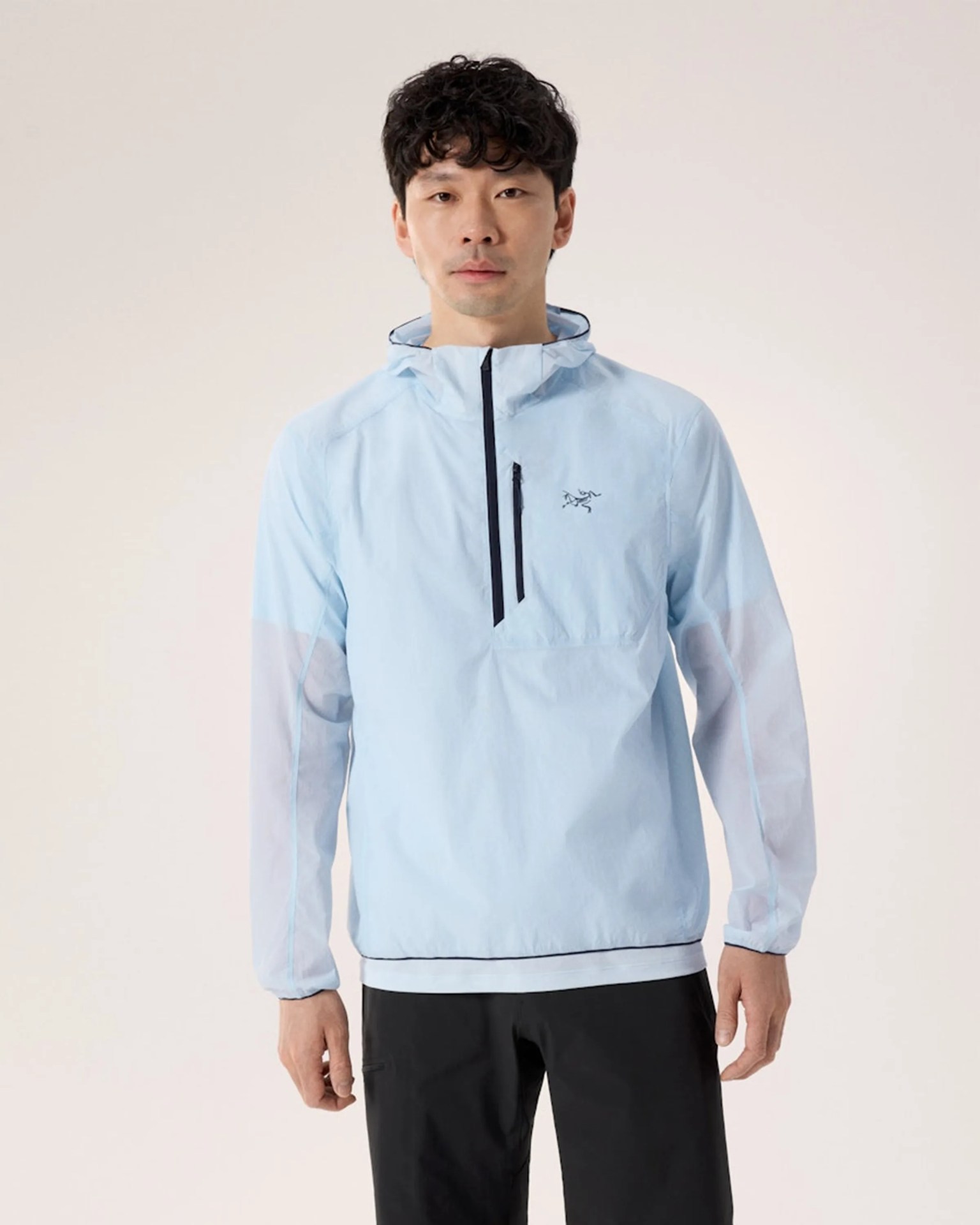 Light blue pullover windbreaker jacket with a front chest zipper pocket and hood worn by a person.