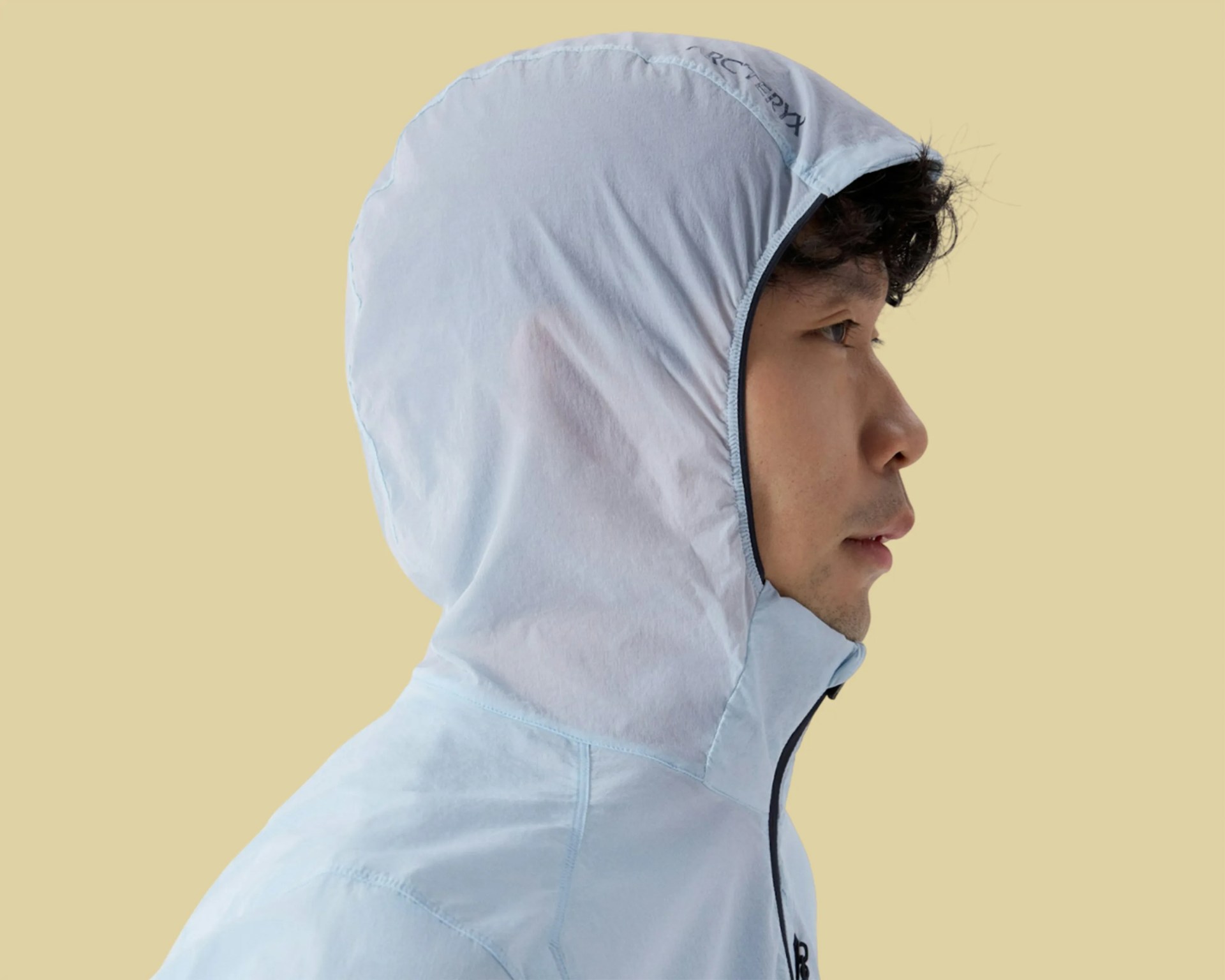 Light blue hooded jacket with a zipper worn by a person in profile against a beige background.