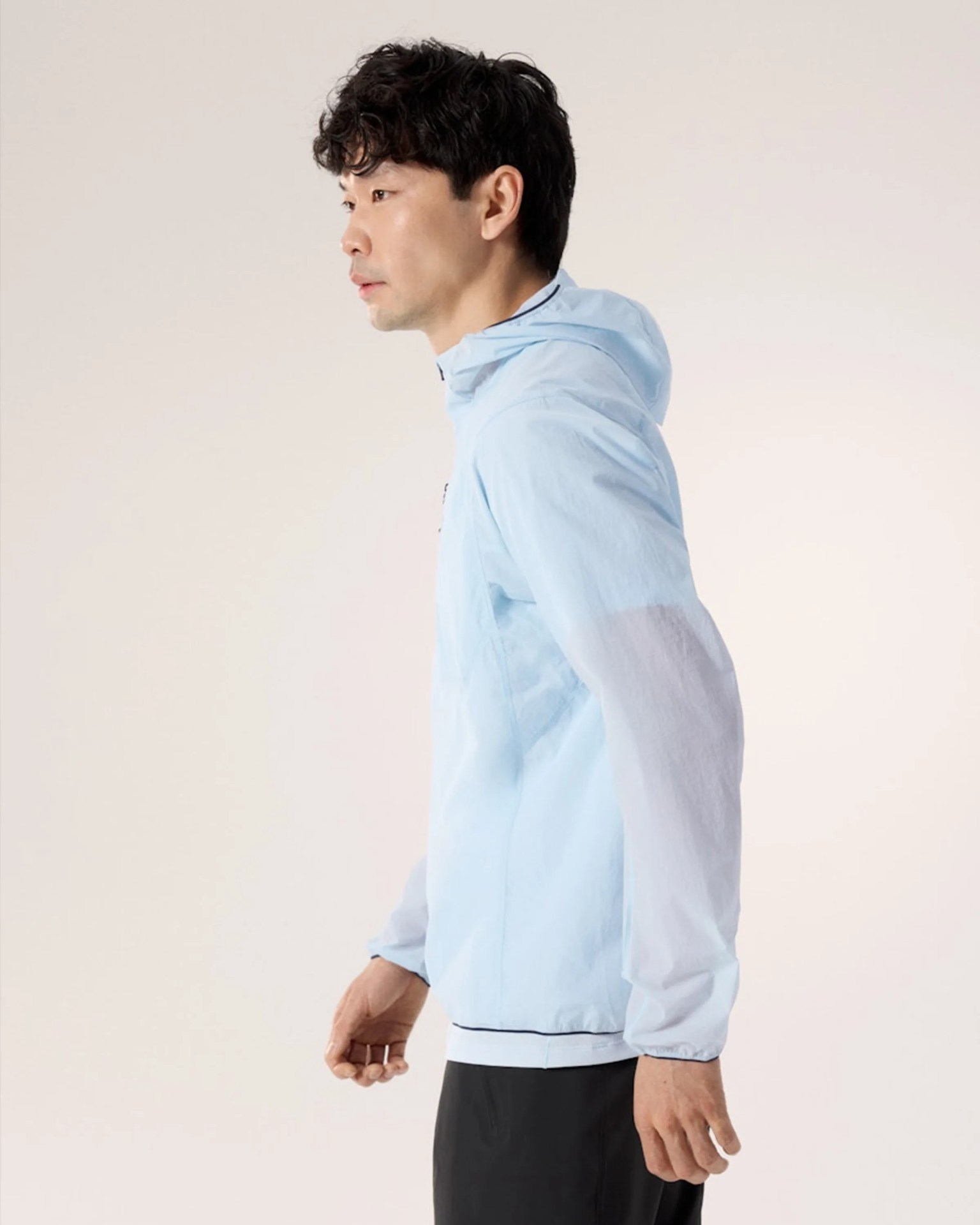 Man wearing a light blue hooded jacket with elastic cuffs and black pants against a plain background.