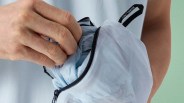Hand placing light blue fabric into a light blue zippered pouch with an Arc'teryx logo tab.