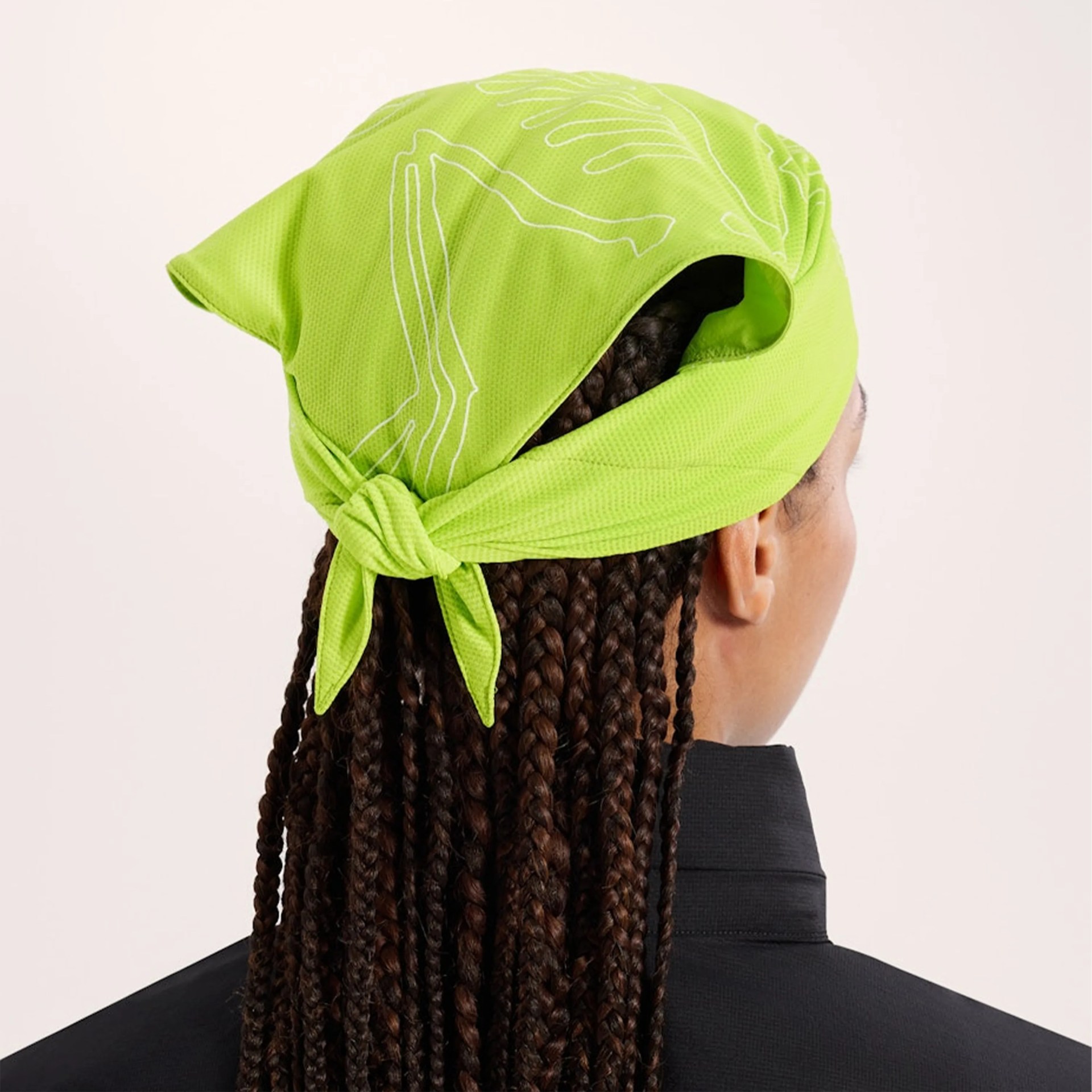 Bright green bandana with white line art tied at the back of a person's head with braided hair.
