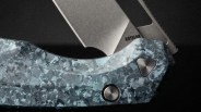Close-up of a folding knife with a blue patterned handle and a partially visible blade marked "ARTISAN.