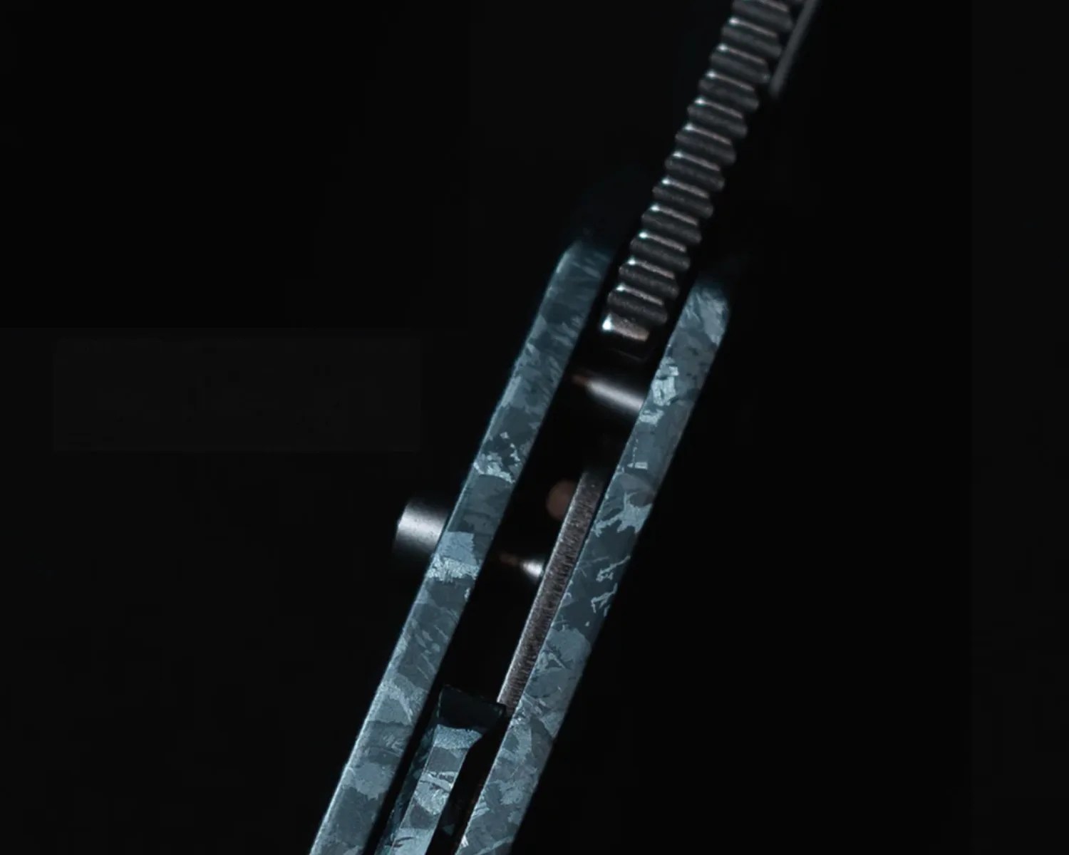 Close-up of a textured blue-gray folding knife spine and locking mechanism against a black background.