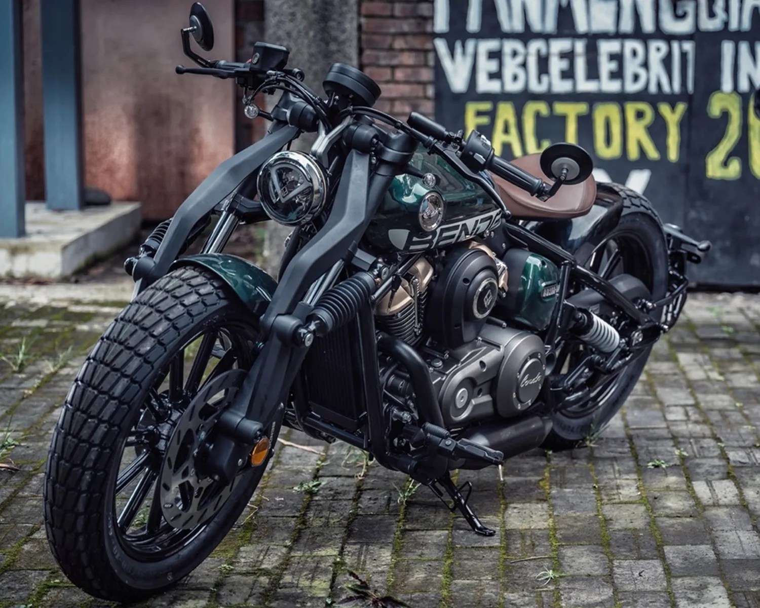 Green and black custom motorcycle with brown leather seat parked on cobblestone pavement.