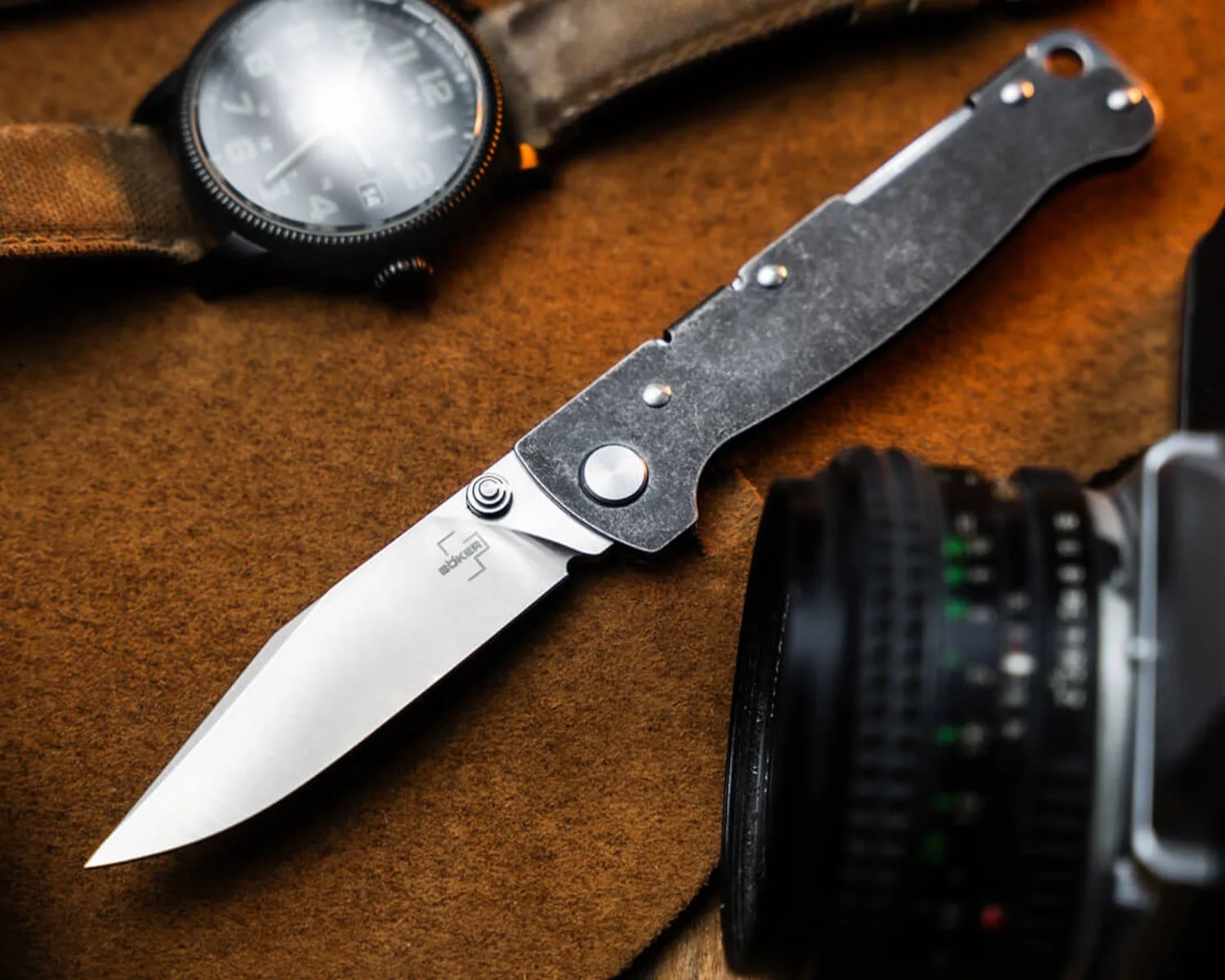 Folding knife with a stonewashed metal handle and a silver blade on a brown fabric surface.