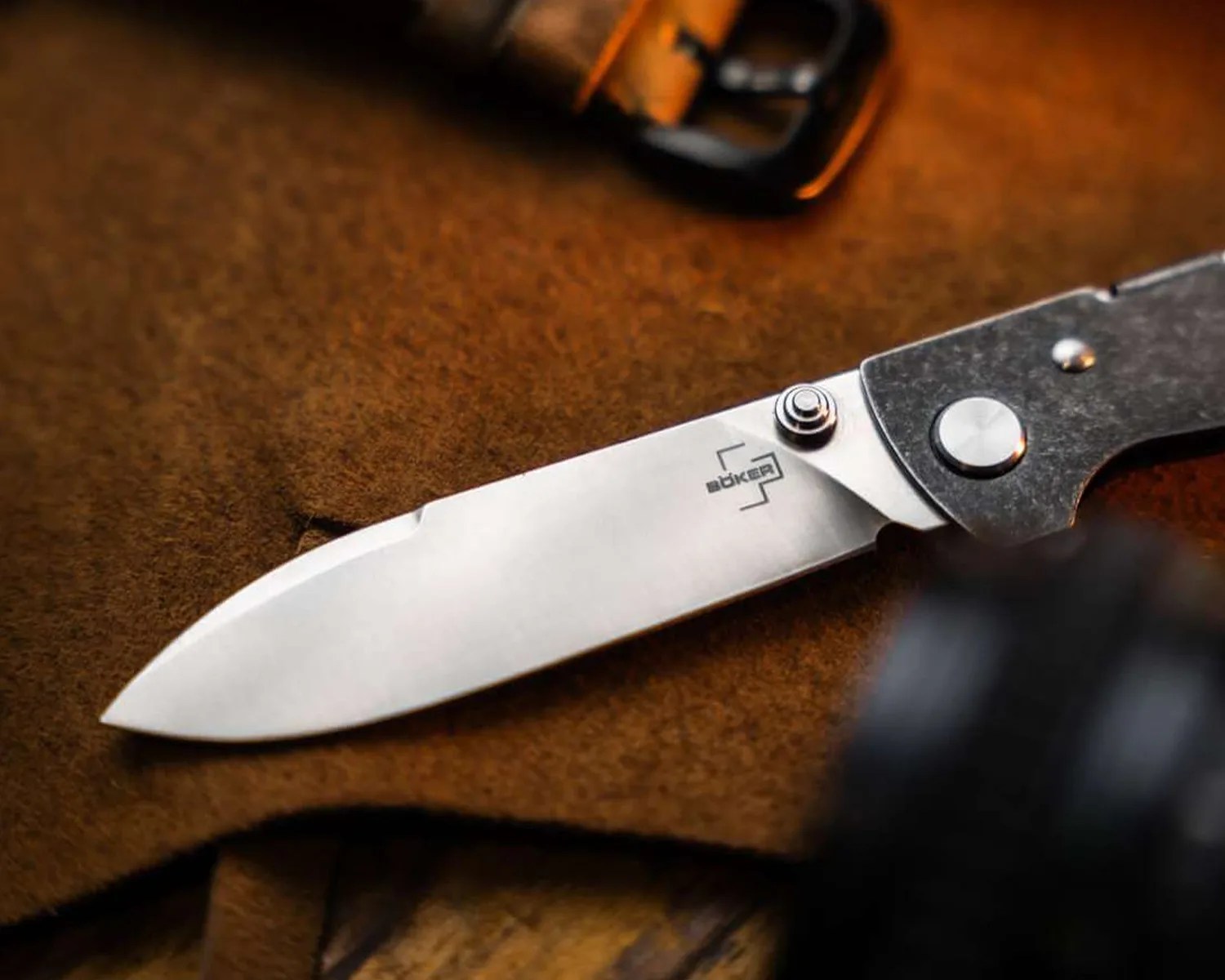 Folding knife with a stainless steel blade and black handle resting on brown fabric.