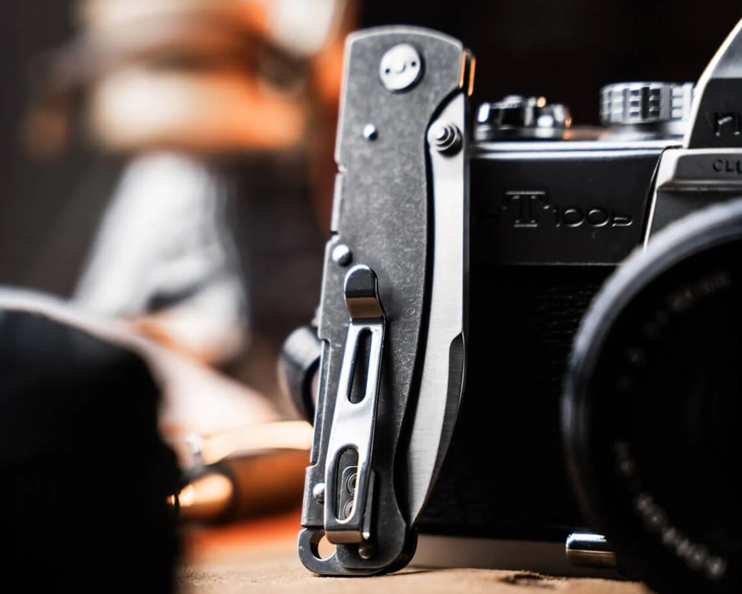 Folded stainless steel pocket knife with a clip standing upright next to a vintage camera.