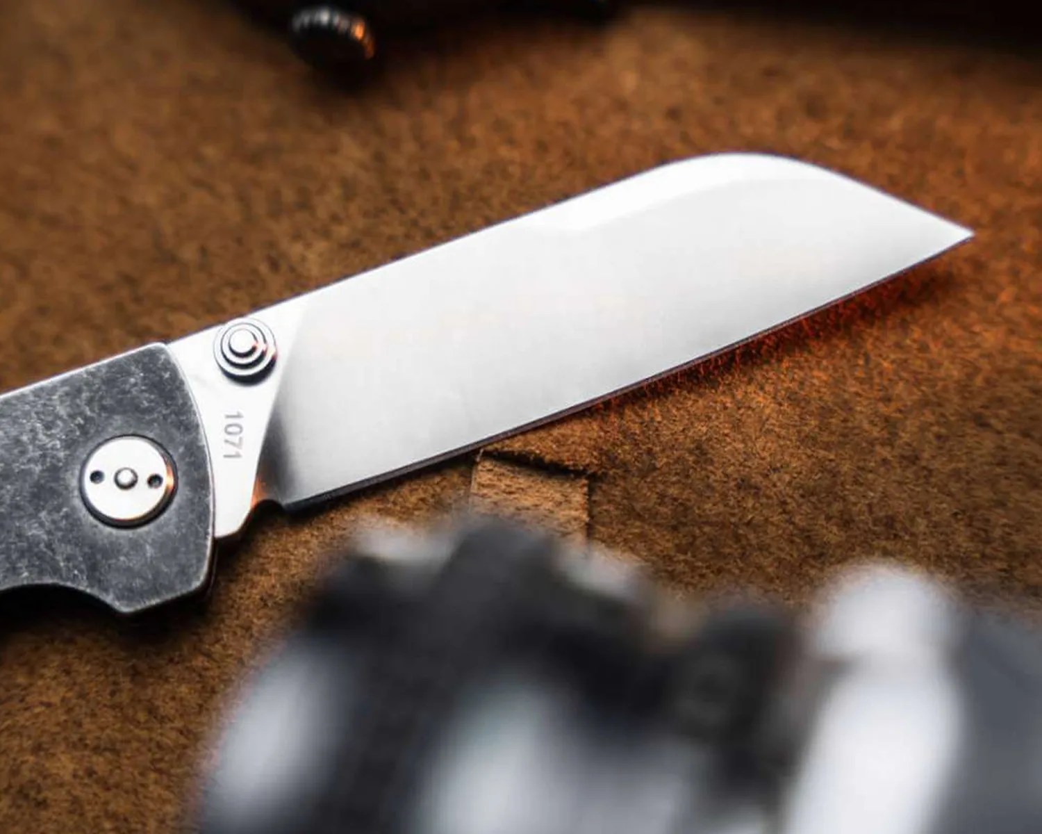 Folding knife with a straight-edged stainless steel blade marked "1071" and a textured dark handle on a brown surface.