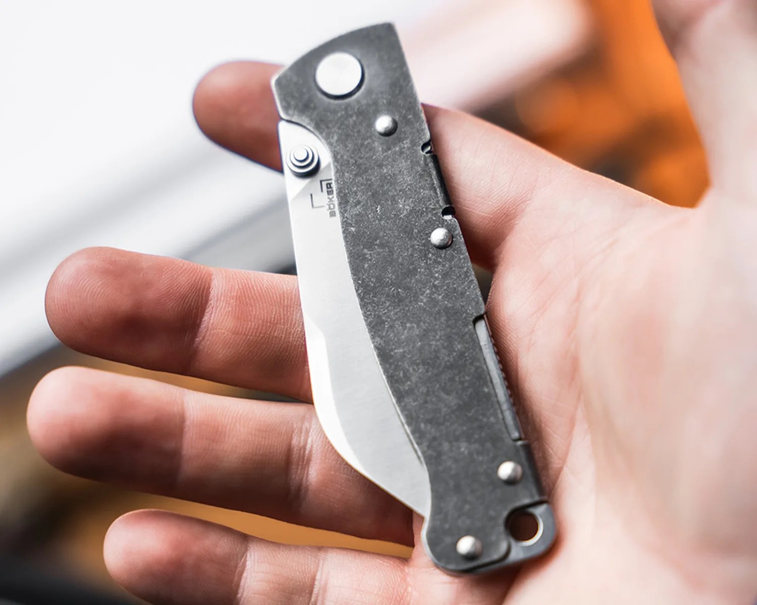 Compact folding pocket knife with a stonewashed metal handle held in a hand.