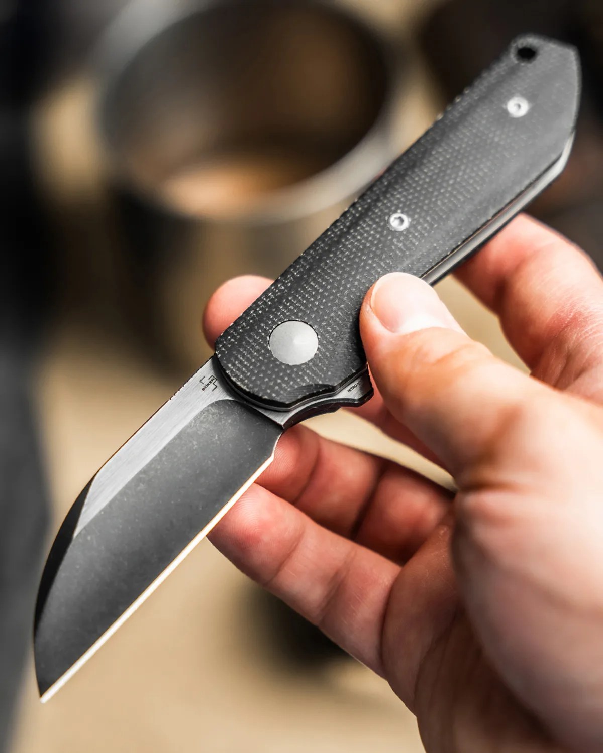 Hand holding a folding knife with a black textured handle and a partially open matte blade.