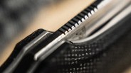 Close-up of a metallic object with a serrated edge and textured black surface.