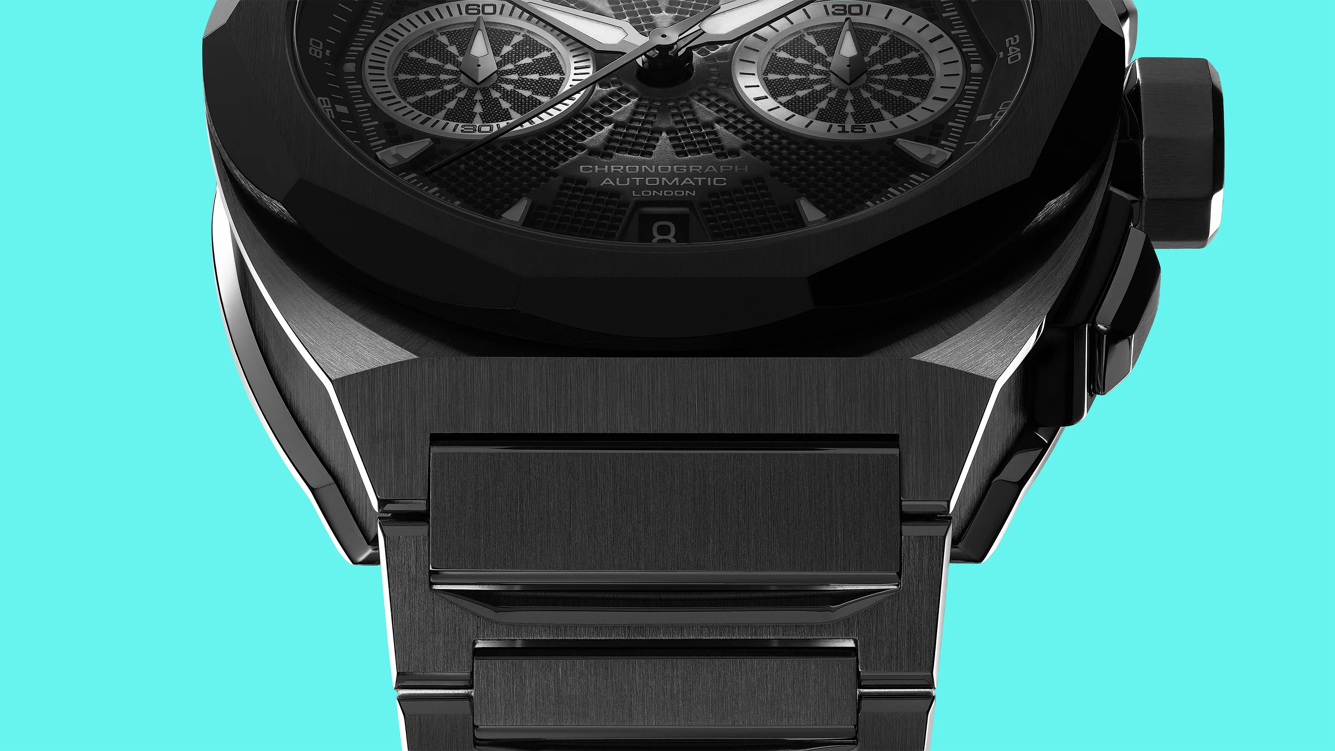 Close-up of a black metal chronograph watch with a textured dial and a linked bracelet against a turquoise background.