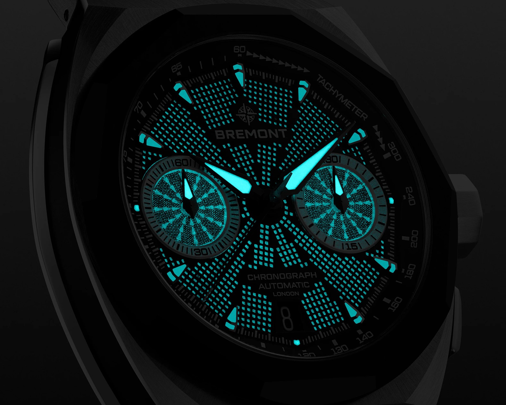 Close-up of a Bremont chronograph watch face with glowing blue luminescent hands and markers in a dark setting.
