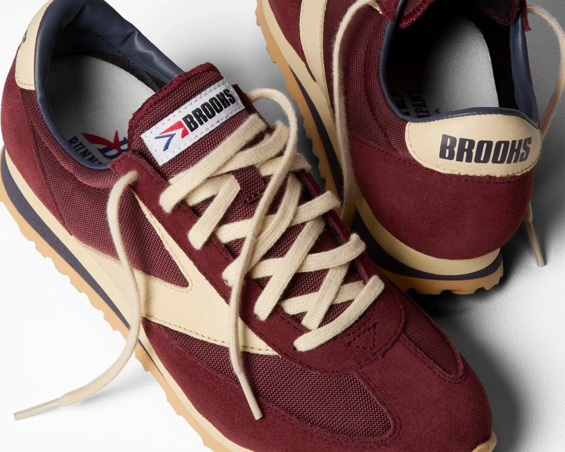 Pair of maroon and beige Brooks running shoes with cream laces and gum soles on a white background.
