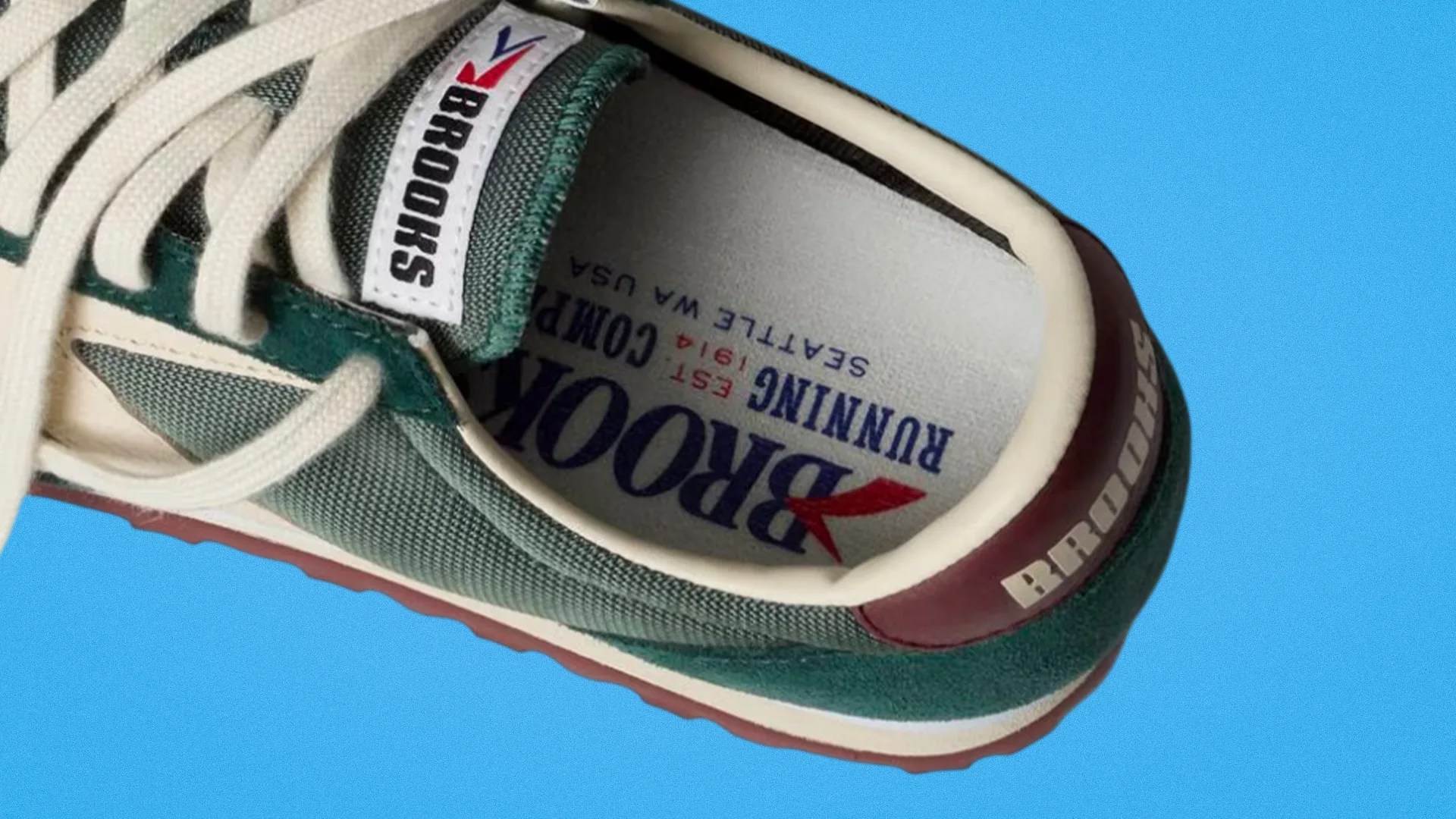 Green and white Brooks running shoe with white laces and red sole on a blue background.