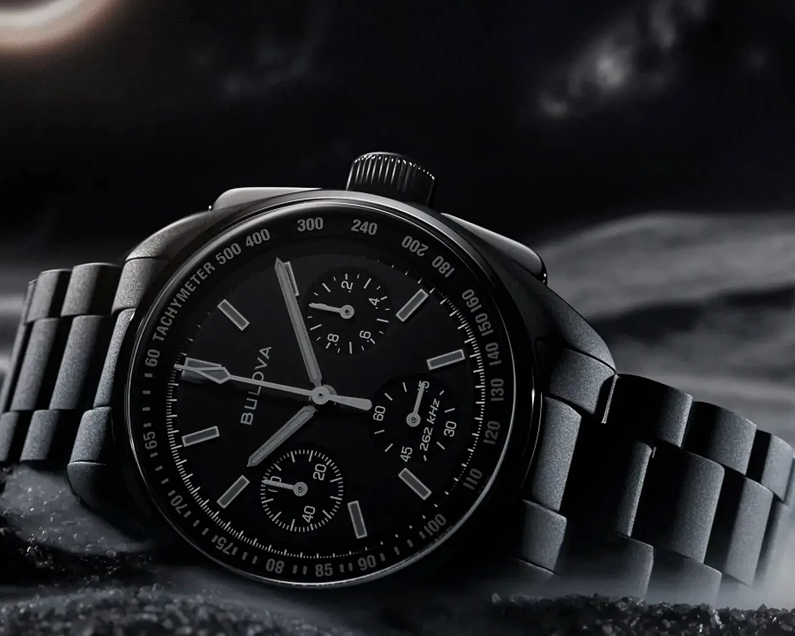 Black Bulova chronograph watch with tachymeter bezel and metal link bracelet on a dark surface.