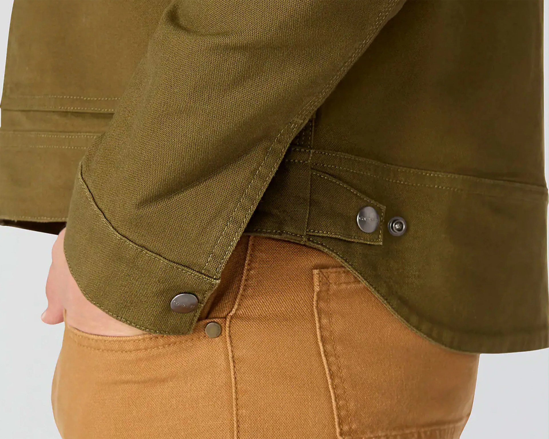 Close-up of olive green jacket cuff with metal snap button over tan pants pocket.
