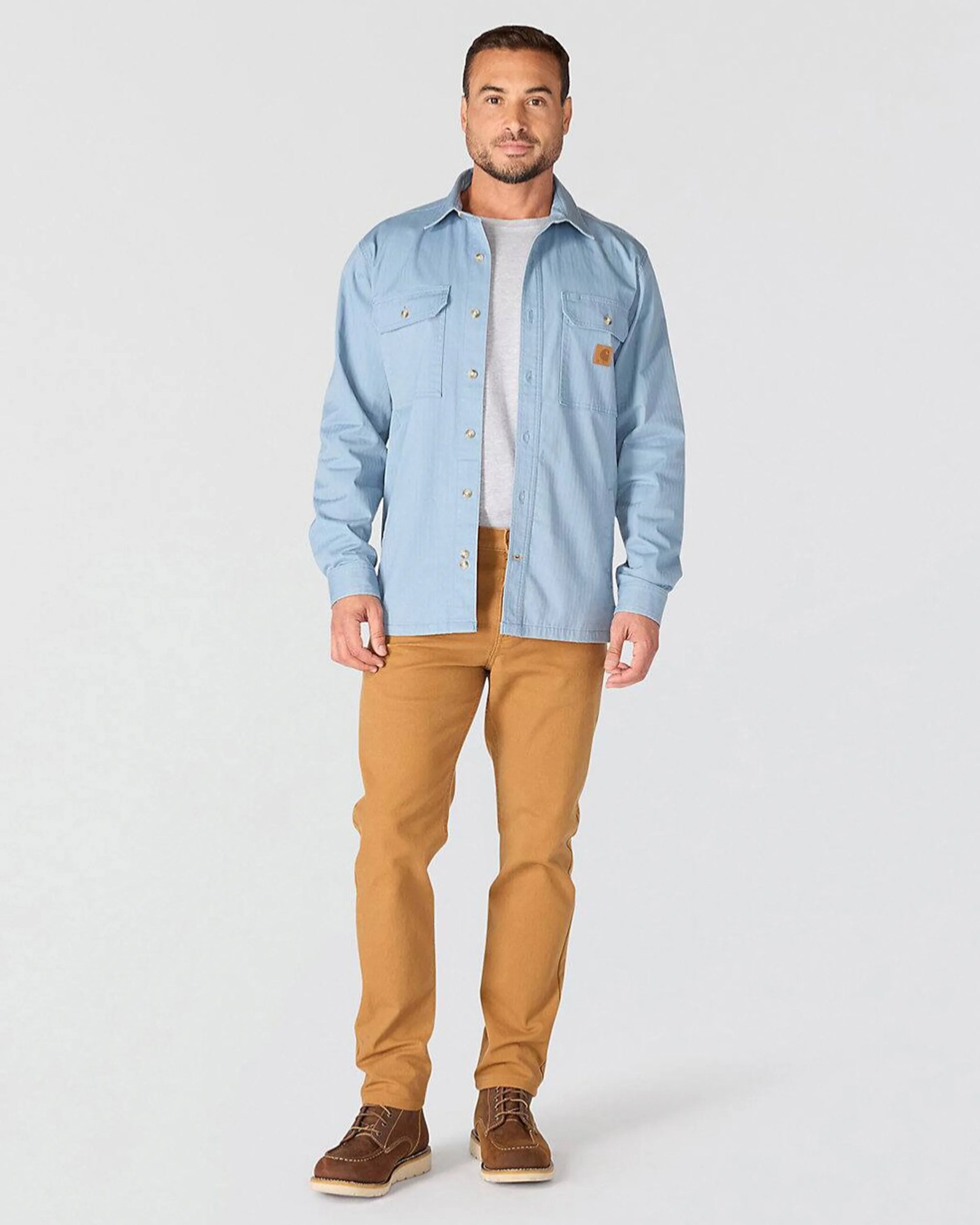 Man wearing light blue button-up shirt over gray t-shirt, tan pants, and brown lace-up boots.