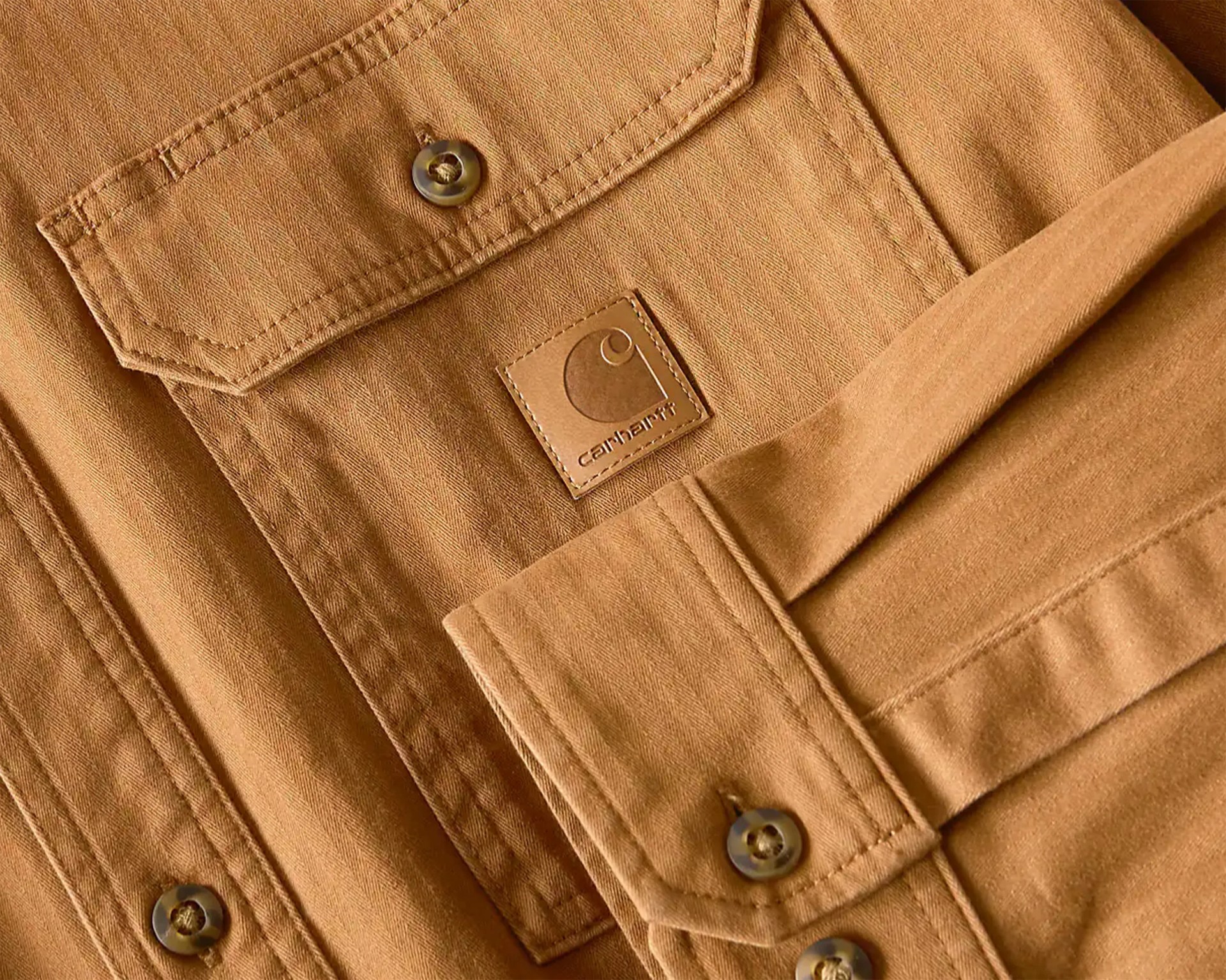 Close-up of a brown Carhartt jacket pocket with button closure and stitched logo patch.