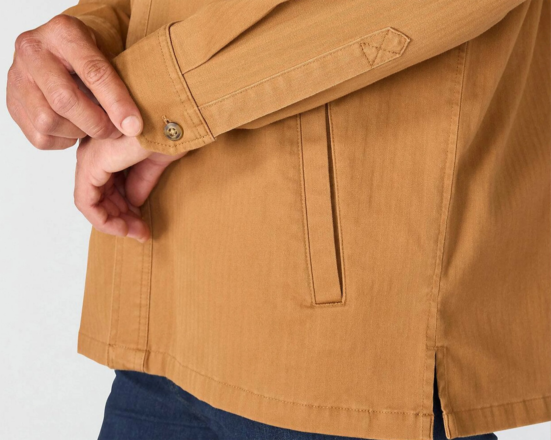 Close-up of a person adjusting the buttoned cuff of a tan jacket with a vertical slit pocket and side vent.