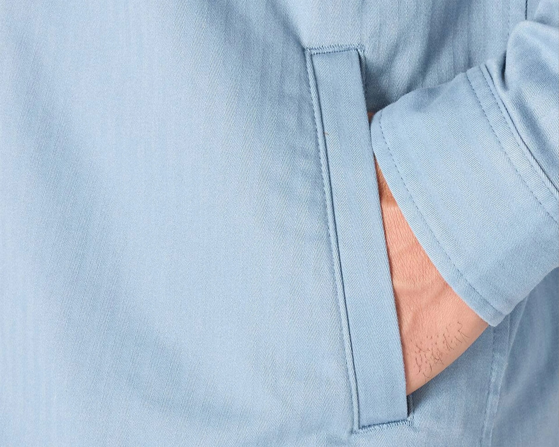 Light blue herringbone fabric jacket pocket with a hand partially inside.