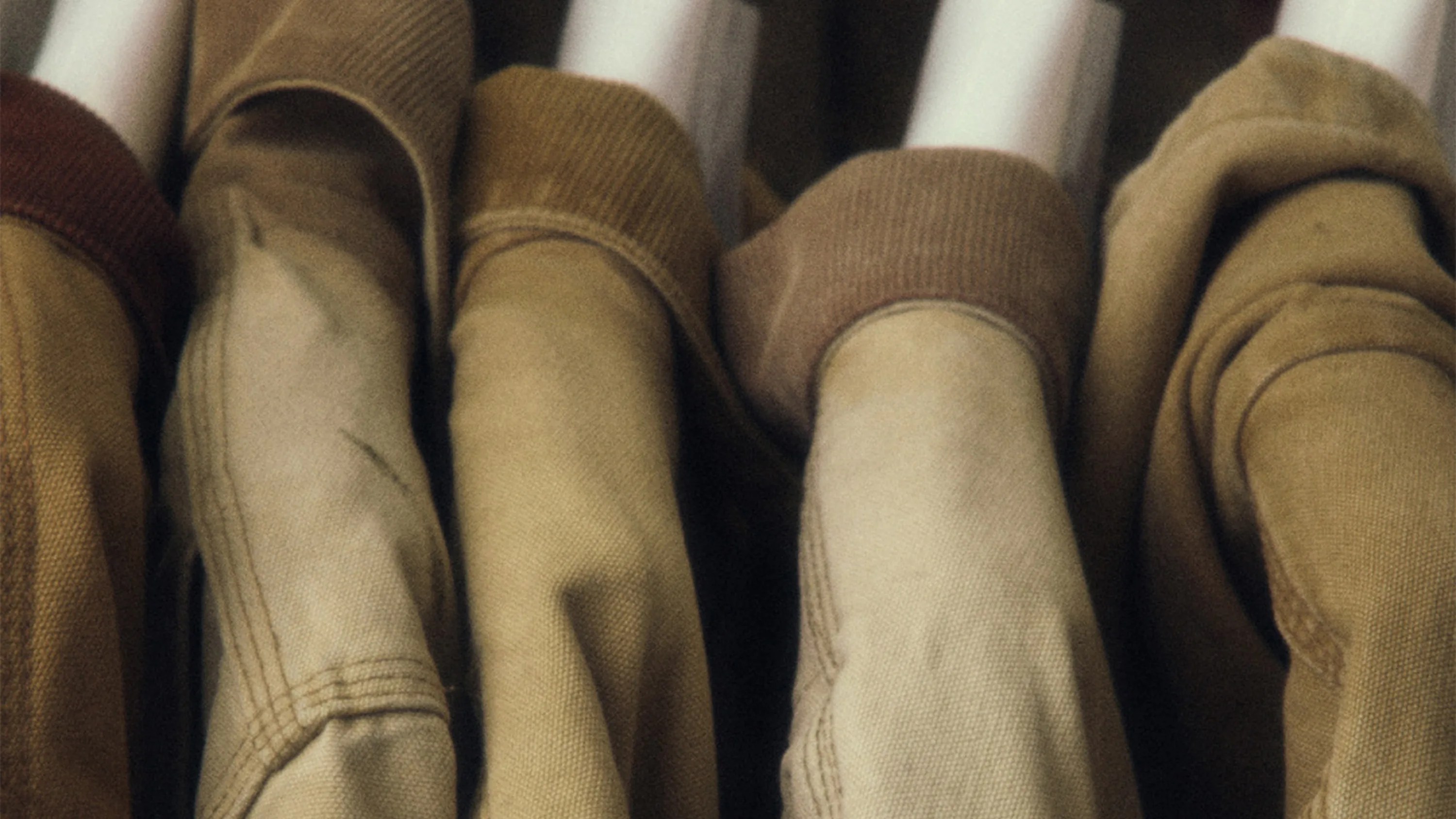 Close-up of several earth-toned jackets hanging on white hangers.