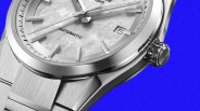 Close-up of a silver automatic wristwatch with a textured dial and date display on a blue background.