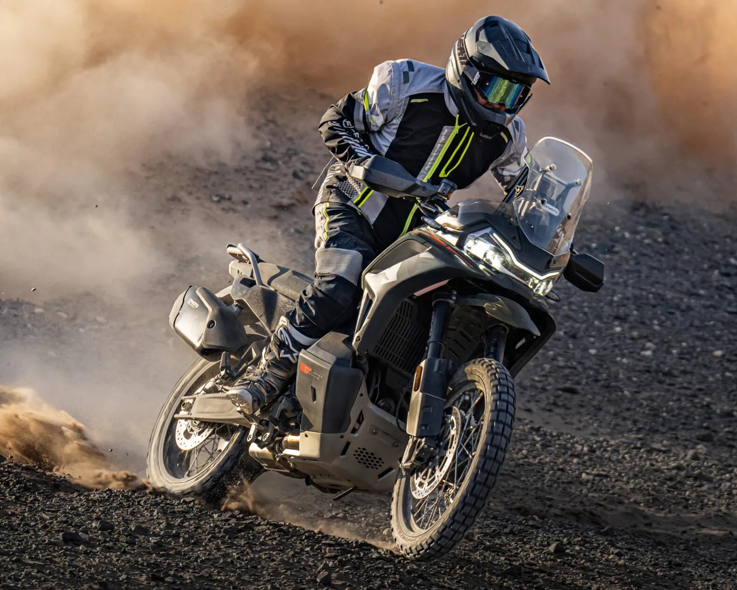 Motorcyclist in black and gray gear riding a black adventure motorcycle on rocky terrain kicking up dust.