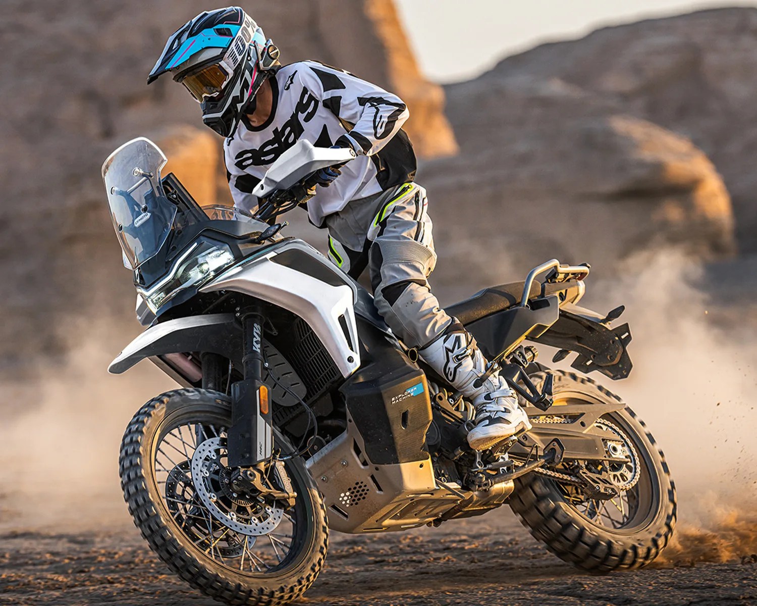 Motorcyclist in white and black gear riding a white and black KTM adventure bike on a dirt trail.