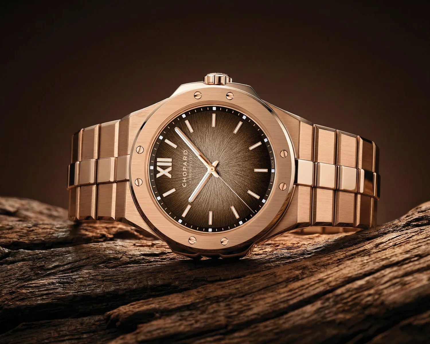 Rose gold Chopard wristwatch with a brown textured dial and metal link bracelet on a wooden surface.