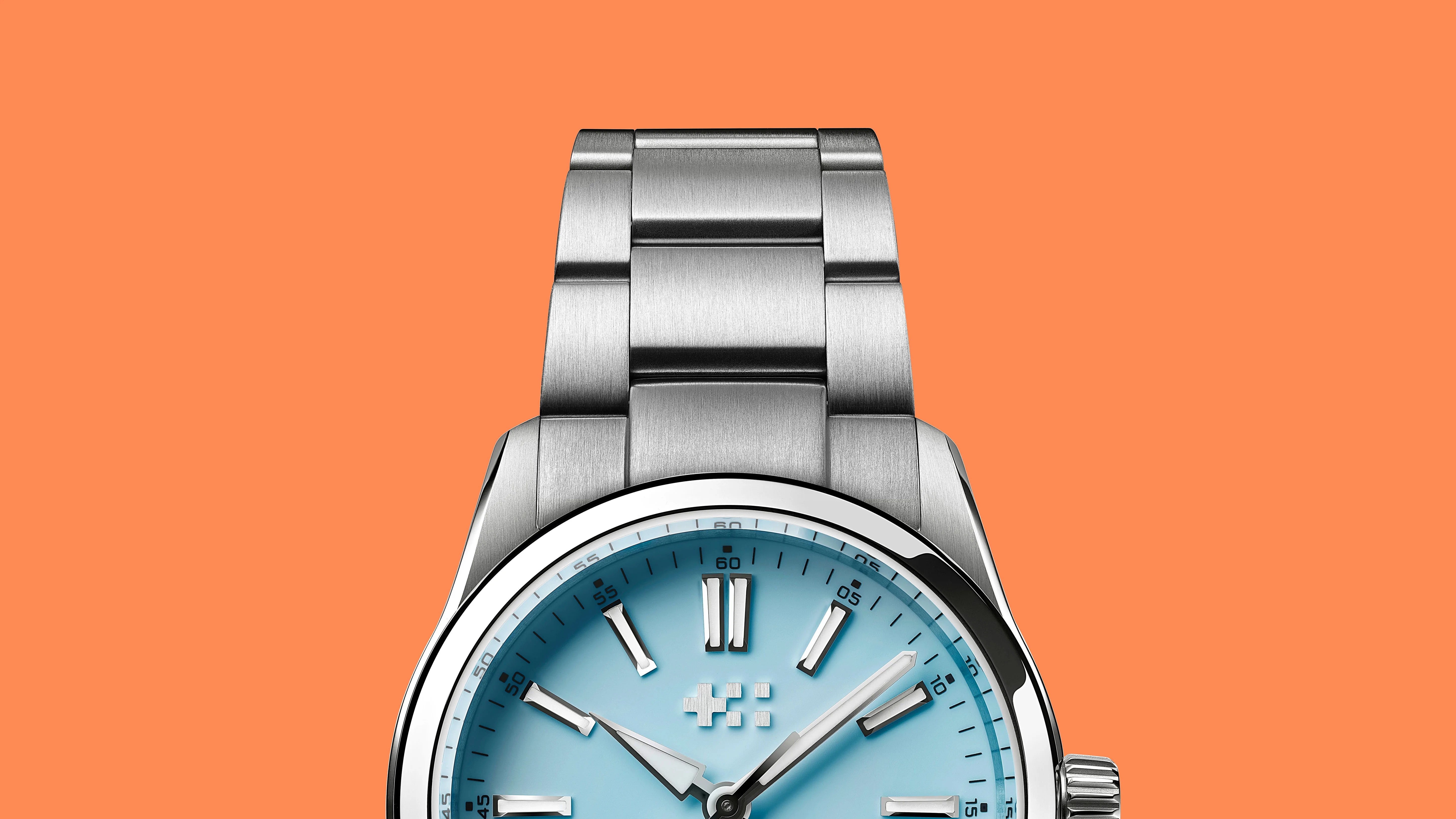 Close-up of a silver metal watch band and light blue watch face with silver hour markers on an orange background.