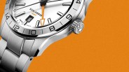 Close-up of a silver stainless steel Sealander GMT watch with white dial and orange GMT hand on an orange background.