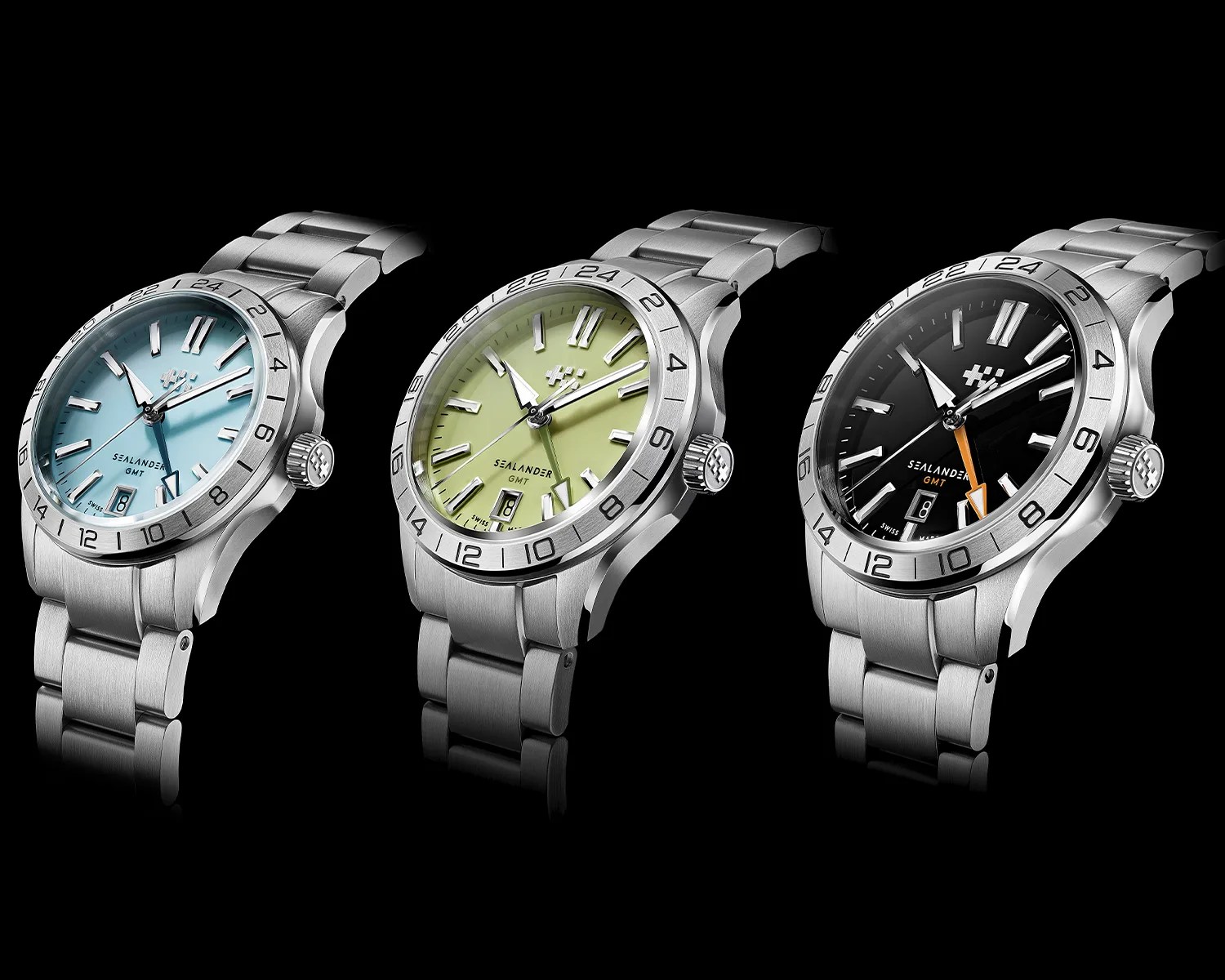 Three stainless steel wristwatches with GMT bezels and pastel blue, light green, and black dials on a black background.