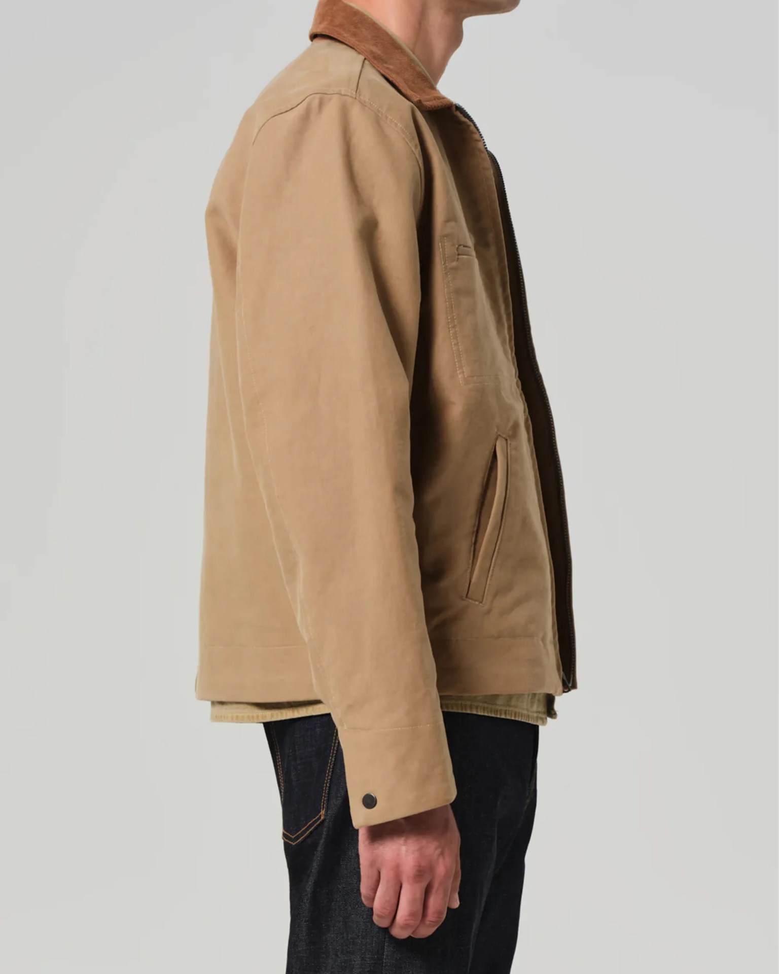 Side view of a person wearing a tan canvas jacket with a brown collar and dark jeans.
