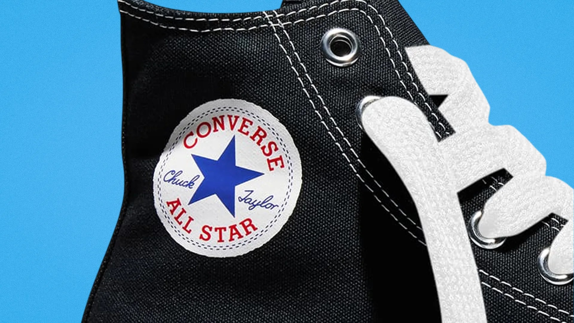Close-up of black Converse All Star sneaker with white laces and blue star logo patch on a blue background.