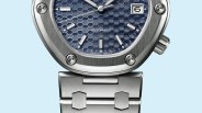 Close-up of a silver metal watch with a blue hexagonal patterned dial, white hour markers, and a date window at 3 o'clock.