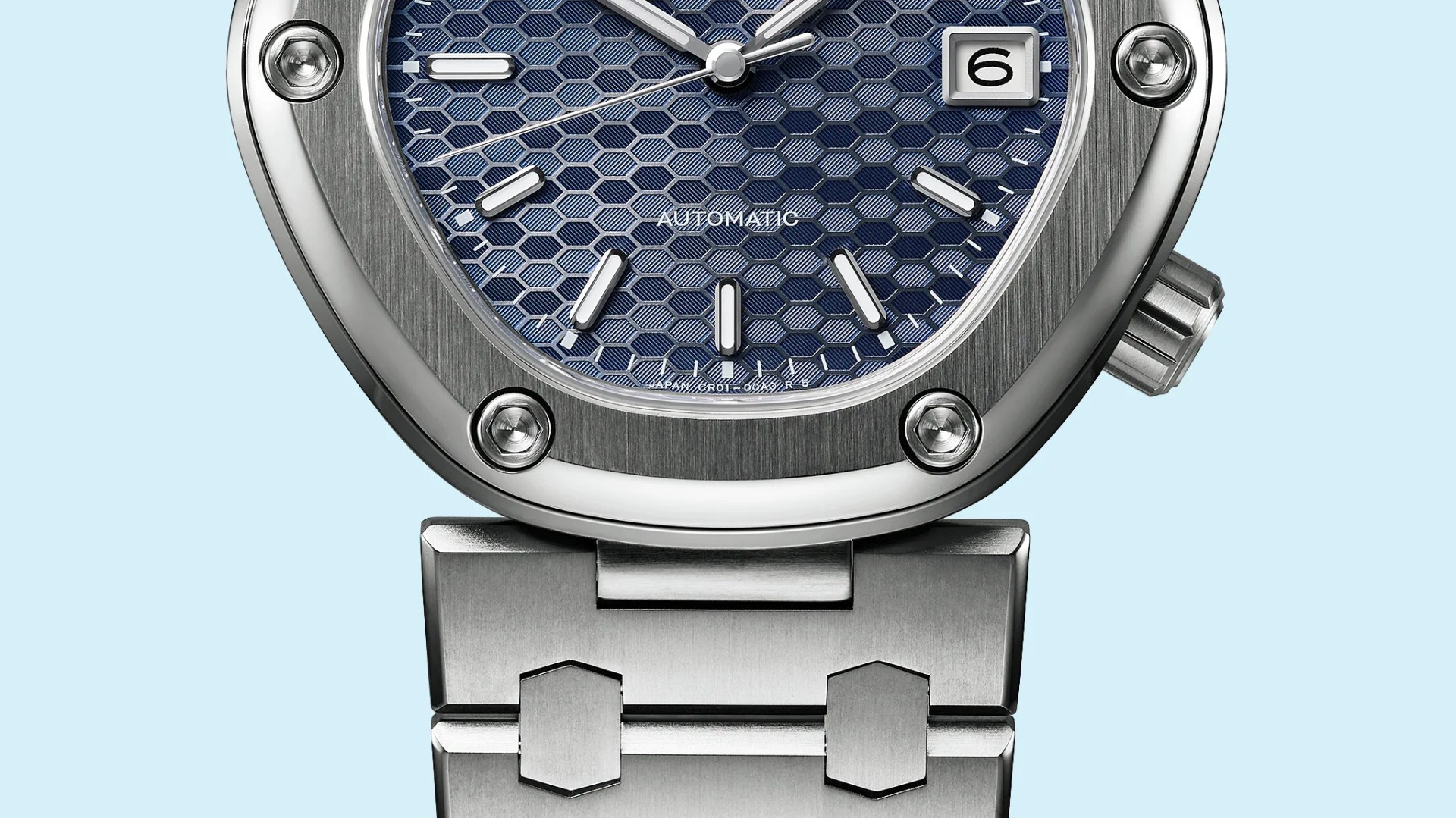 Close-up of a silver metal watch with a blue hexagonal patterned dial, white hour markers, and a date window at 3 o'clock.